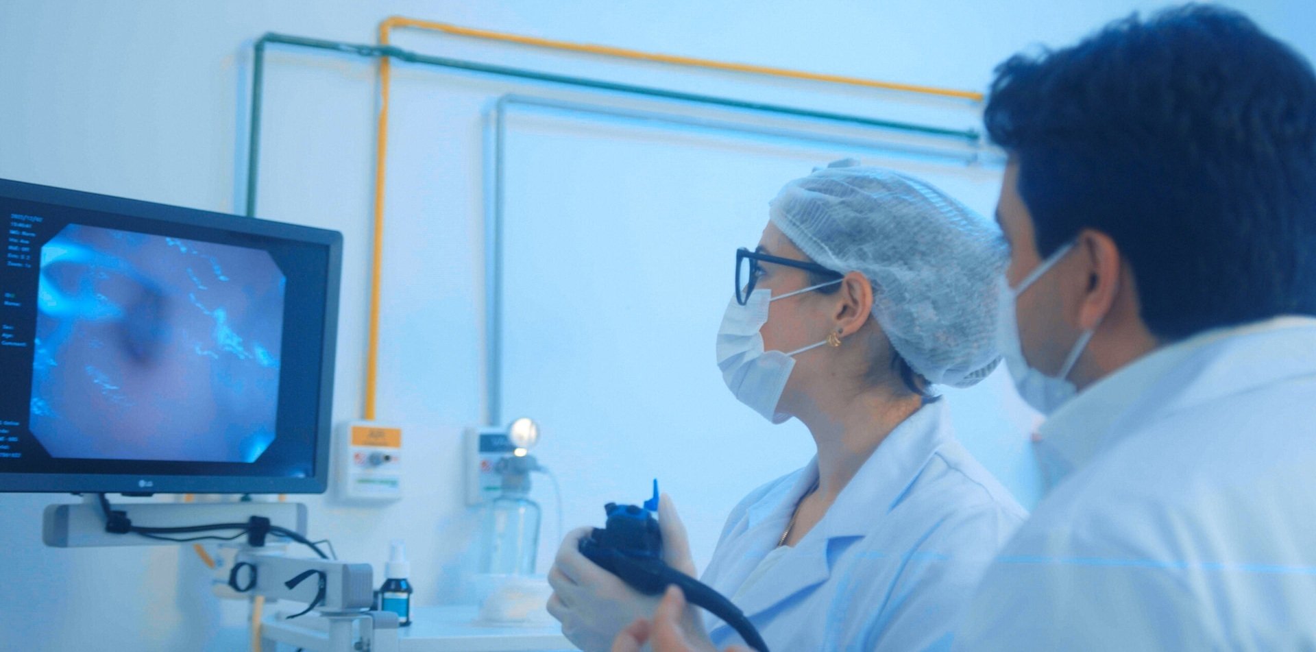 Médicos acompanham imagens de exame de endoscopia digestiva em monitor durante procedimento realizado em ambiente clínico.
